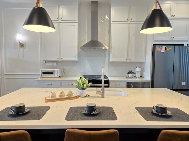 kitchen featuring wall chimney range hood, freestanding refrigerator, light stone countertops, tasteful backsplash, and pendant lighting