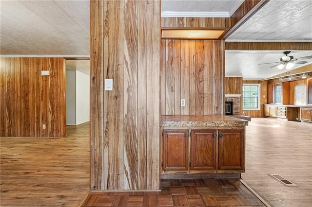 kitchen with crown molding, ceiling fan, dark parquet floors, a brick fireplace, and wood walls