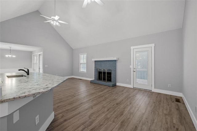 unfurnished living room featuring sink, a fireplace, ceiling fan with notable chandelier, dark hardwood / wood-style flooring, and high vaulted ceiling