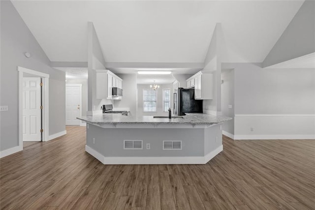 kitchen with kitchen peninsula, white cabinets, hardwood / wood-style flooring, and vaulted ceiling