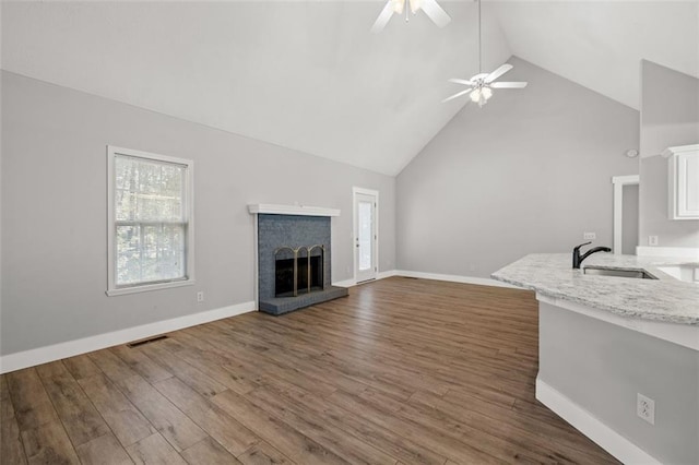 unfurnished living room with sink, dark hardwood / wood-style flooring, a fireplace, high vaulted ceiling, and ceiling fan