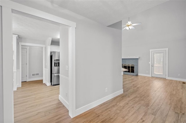 unfurnished living room featuring light hardwood / wood-style floors, a textured ceiling, and a brick fireplace