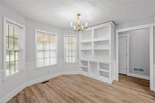 unfurnished dining area featuring light hardwood / wood-style floors, a notable chandelier, and a textured ceiling