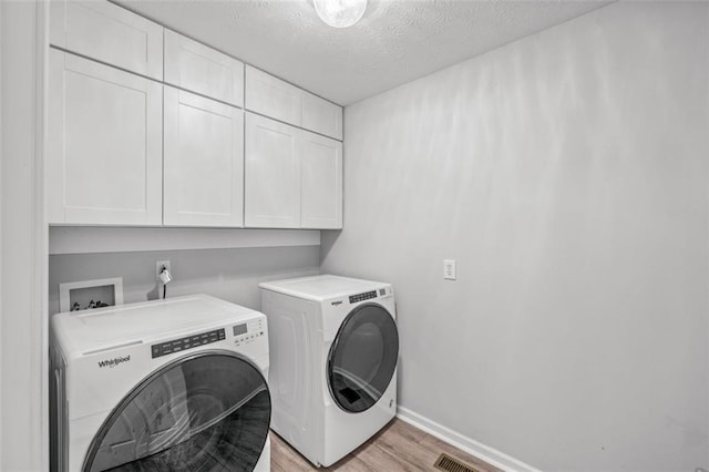 laundry room with light hardwood / wood-style flooring, independent washer and dryer, a textured ceiling, and cabinets