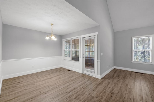 unfurnished dining area featuring lofted ceiling, light hardwood / wood-style flooring, and a notable chandelier