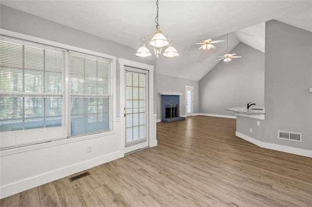 unfurnished living room featuring a healthy amount of sunlight, lofted ceiling, ceiling fan with notable chandelier, and hardwood / wood-style floors