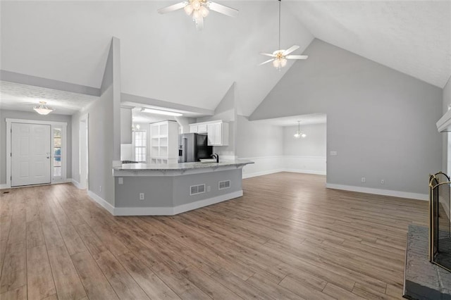 unfurnished living room with light hardwood / wood-style flooring, a fireplace, high vaulted ceiling, and ceiling fan