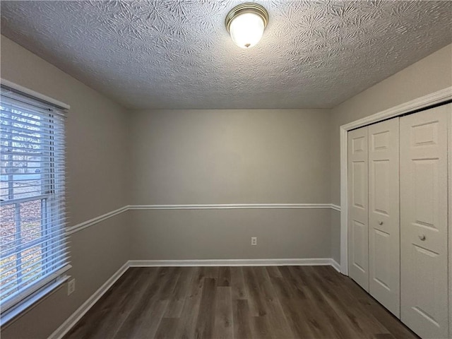 unfurnished bedroom featuring multiple windows, dark wood-type flooring, a textured ceiling, and a closet