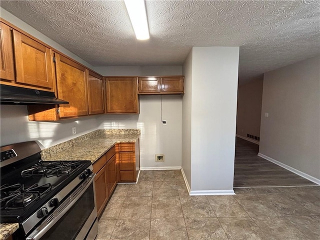 kitchen featuring light stone counters, stainless steel gas range, tile patterned flooring, and a textured ceiling