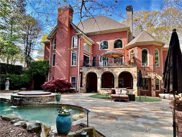 rear view of house with brick siding, a chimney, a balcony, a patio area, and an in ground hot tub