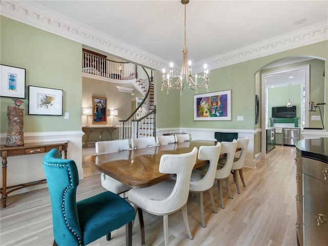 dining space with arched walkways, light wood-style flooring, stairs, and crown molding