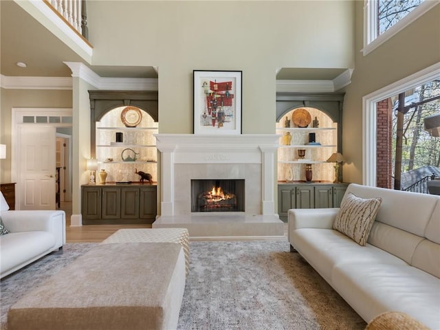 living room featuring visible vents, built in shelves, crown molding, a premium fireplace, and a towering ceiling