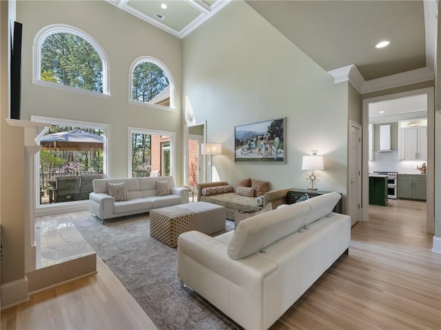 living room featuring recessed lighting, a high ceiling, ornamental molding, and light wood finished floors