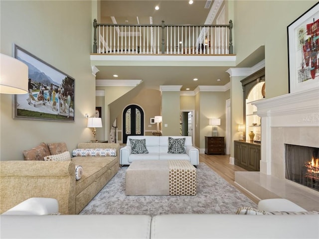 living room with wood finished floors, a premium fireplace, a high ceiling, recessed lighting, and crown molding