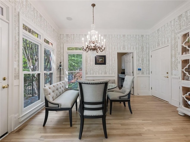 dining room featuring light wood finished floors, wallpapered walls, a chandelier, ornamental molding, and wainscoting