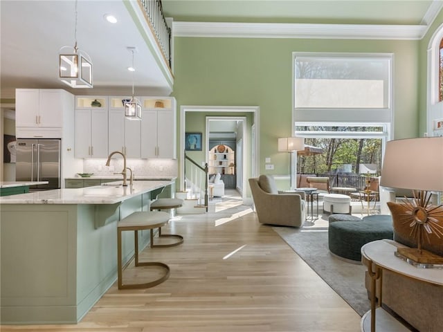 kitchen with crown molding, stainless steel built in fridge, light wood-style flooring, a towering ceiling, and white cabinetry