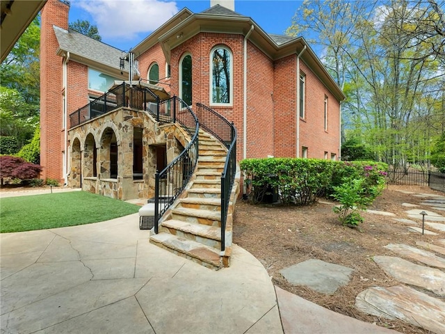 view of front of home featuring stairs, a front yard, brick siding, and a chimney