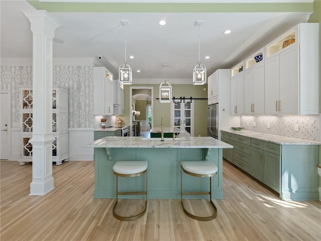 kitchen with a center island with sink, a sink, a barn door, crown molding, and wallpapered walls