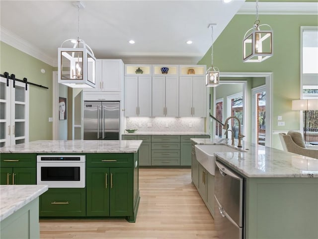 kitchen featuring a sink, green cabinetry, ornamental molding, stainless steel appliances, and a kitchen island with sink