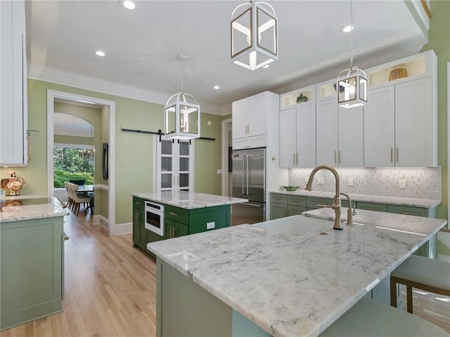 kitchen with green cabinetry, built in refrigerator, a kitchen island with sink, and ornamental molding