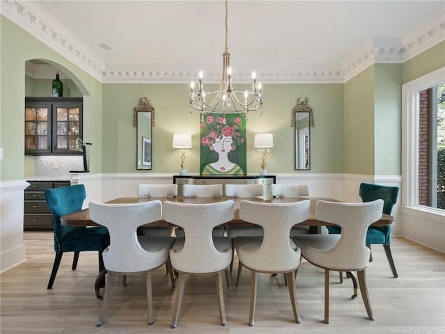 dining space with a wainscoted wall, a chandelier, crown molding, and light wood finished floors