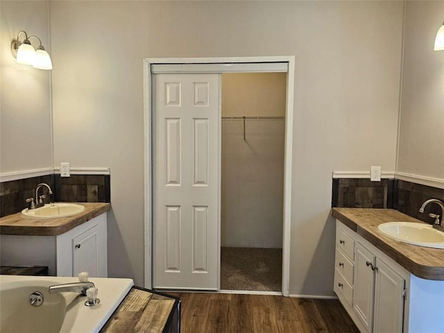 full bath featuring two vanities, a walk in closet, a sink, and wood finished floors