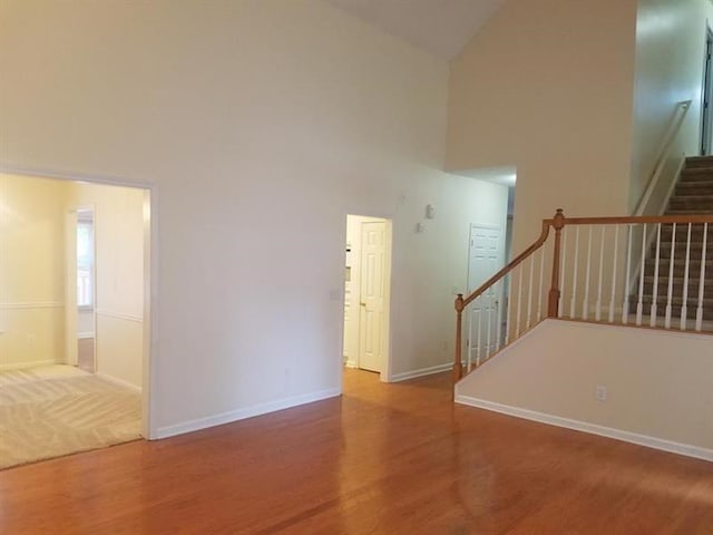 unfurnished living room with stairway, high vaulted ceiling, baseboards, and wood finished floors