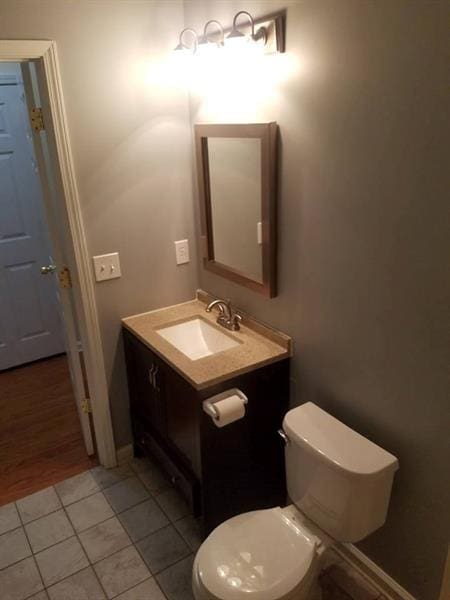 half bath with vanity, baseboards, tile patterned floors, and toilet