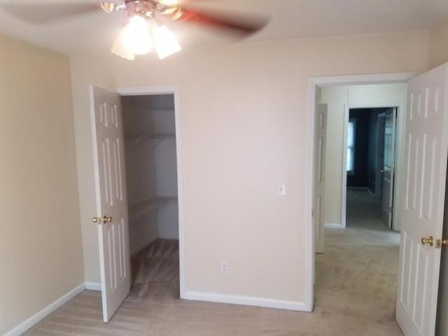 unfurnished bedroom with light carpet, a ceiling fan, baseboards, a spacious closet, and a closet