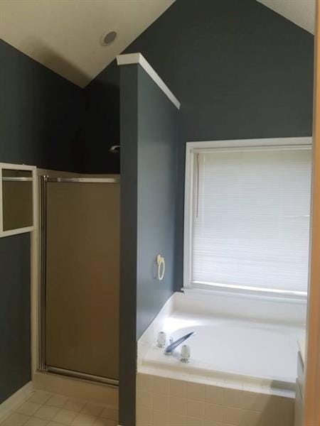 bathroom featuring a bath, a stall shower, and vaulted ceiling