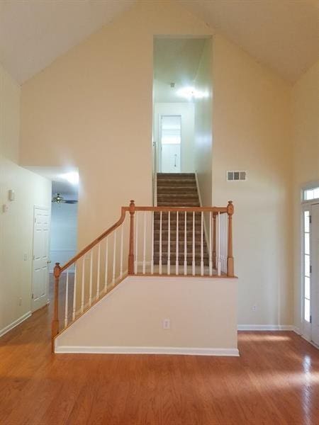 stairs featuring baseboards, high vaulted ceiling, visible vents, and wood finished floors