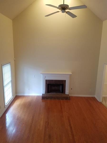 unfurnished living room featuring ceiling fan, a brick fireplace, wood finished floors, high vaulted ceiling, and baseboards