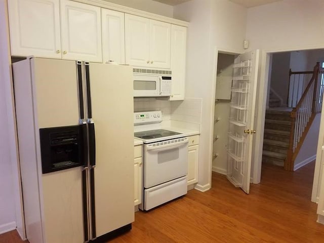 kitchen featuring backsplash, light countertops, white cabinets, light wood finished floors, and white appliances