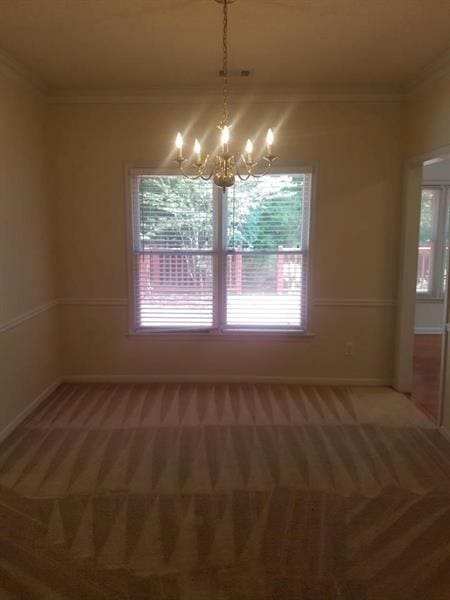 unfurnished dining area featuring baseboards, ornamental molding, light carpet, and a chandelier