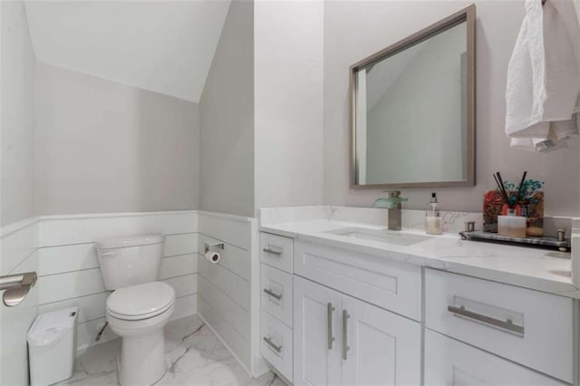 bathroom featuring a wainscoted wall, toilet, vaulted ceiling, marble finish floor, and vanity