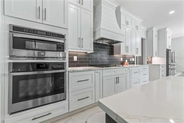 kitchen with tasteful backsplash, light stone countertops, premium range hood, and stainless steel appliances