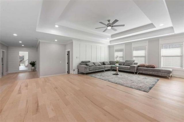 living room with ceiling fan, a raised ceiling, light wood-style flooring, and ornamental molding