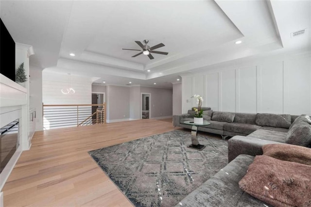 living area with a tray ceiling, a decorative wall, wood finished floors, and visible vents