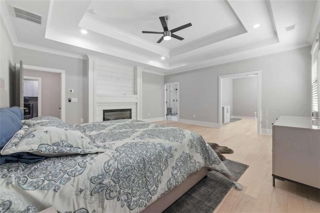 bedroom with a tray ceiling, visible vents, light wood-style flooring, and crown molding