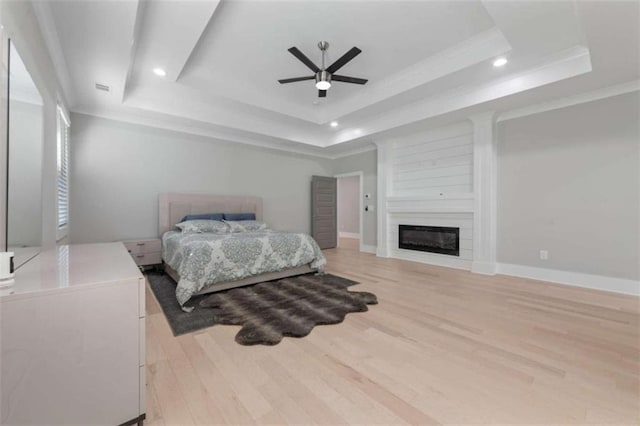 bedroom with baseboards, light wood finished floors, a tray ceiling, recessed lighting, and a fireplace