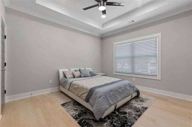 bedroom with visible vents, baseboards, a raised ceiling, and light wood-style floors