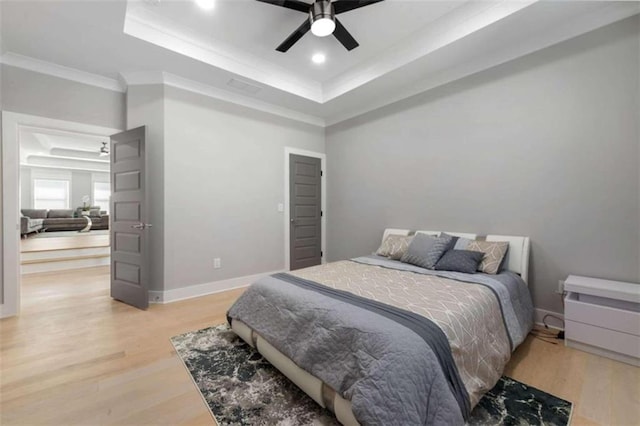 bedroom with a raised ceiling, light wood-style flooring, crown molding, and baseboards