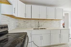 kitchen with stainless steel range with electric stovetop, decorative backsplash, white cabinetry, and sink