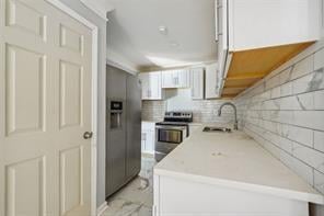 kitchen featuring decorative backsplash, white cabinets, stainless steel appliances, and sink