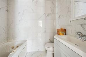 bathroom with tile walls, vanity, toilet, and a tub