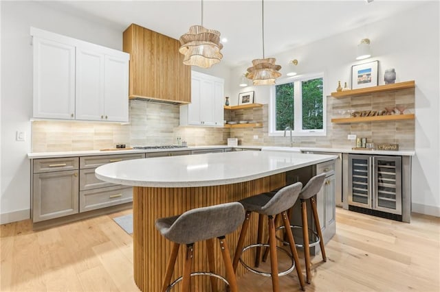 kitchen with decorative backsplash, beverage cooler, white cabinets, a kitchen island, and hanging light fixtures