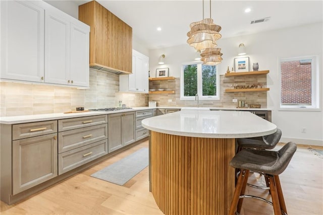 kitchen featuring decorative backsplash, a breakfast bar, a center island, light hardwood / wood-style floors, and hanging light fixtures