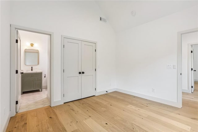 unfurnished bedroom with a closet, light wood-type flooring, high vaulted ceiling, and ensuite bath