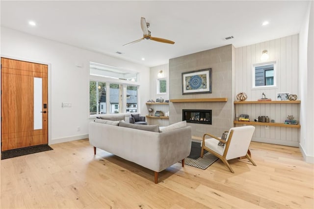 living room featuring ceiling fan, light wood-type flooring, and a tile fireplace