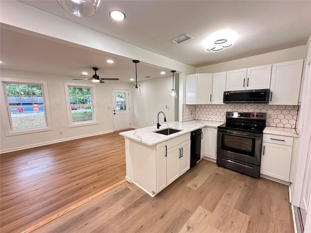 kitchen featuring black appliances, hanging light fixtures, sink, light hardwood / wood-style floors, and kitchen peninsula